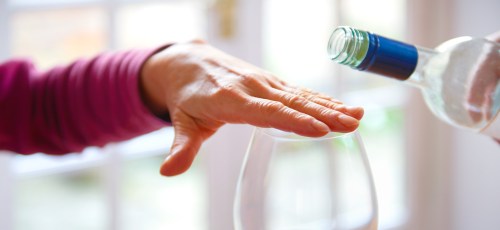 a woman's hand over a wine glass blocking a bottle of wine